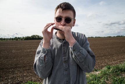 A young white man with brown hair playing a harmonica